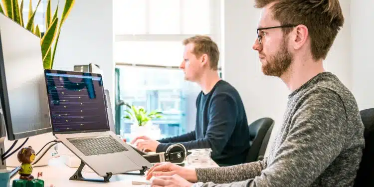 man sitting on chair wearing gray crew-neck long-sleeved shirt using Apple Magic Keyboard